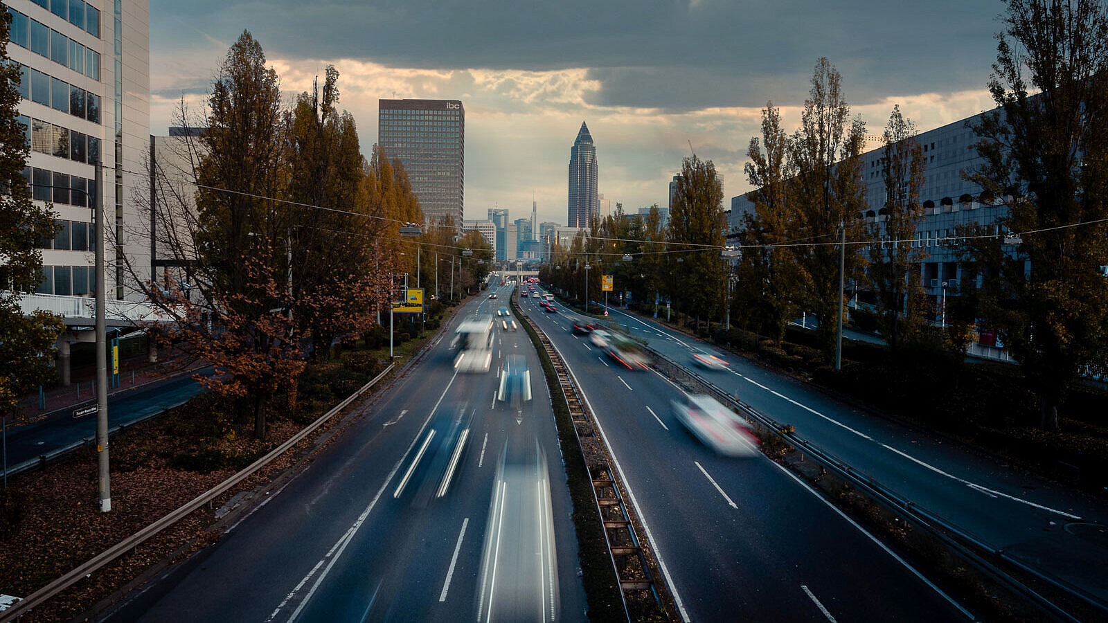vierspurige Straße mit Hochhäusern und dem Messeturm Frankfurt im Hintergrund