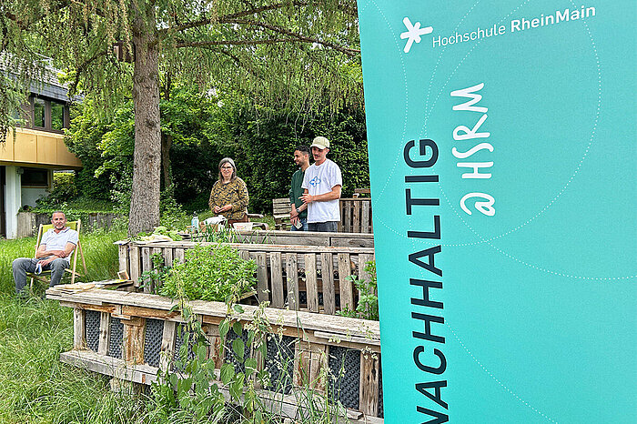 Mitarbeiter des Nachhaltigkeitsbrüs der Hochschule RheinMain stehen gemeinsam mit der Referentin Sybille Fuchs in Kurts Garten auf dem Campus Kurt-Schumacher-Ring der Hochschule RheinMain