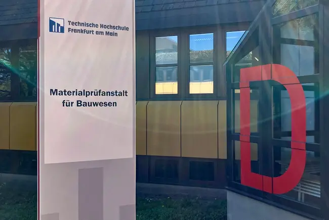 Ein für die Dreharbeiten angebrachtes Schild der fiktiven Technischen Hochschule Frankfurt am Main zeigt die Aufschrift „Materialprüfanstalt für Bauwesen“. Im Hintergrund ist das D-Gebäude der Hochschule RheinMain zu sehen.