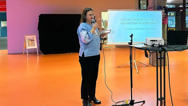 Die ukrainische Gastwissenschaftlerin Prof. Dr. Galyna Nesterenko steht während ihres Vortrags auf dem Länderabend Ukraine mit einem Mikrofon in der Hand vor einer Leinwand, auf der eine Präsentation zur Geschichte der Ukraine zu sehen ist.