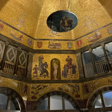 Blick nach oben in die Kuppel der Rotunde des Museum Wiesbaden. Die Flächen sind geschmückt mit glänzendem, goldenem Mosaik und Wappen aus bunten Mosaiksteinen.