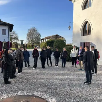 A group of architectural heritage students stand in a semicircle around a speaker and listen. The students are on an excursion to Italy with Professor Dr. Abrihan and are visiting a winery.