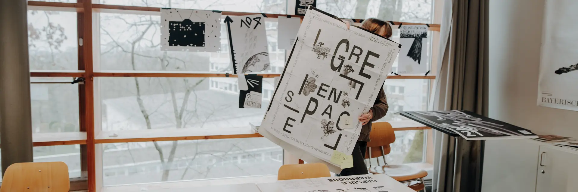 Hinter einem typografischen Plakat steht eine Studierende im Seminarraum