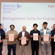 Sechs Teilnehmer halten ihre Zertifikate in die Kamera. Im Hintergrund zeigt ein Bildschirm den Titel „WINTERSCHOOL 2026“ und „Management Skills for Engineers“. Die Atmosphäre ist festlich, und die Teilnehmer scheinen stolz auf ihre Leistungen zu sein.