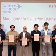 Sechs Teilnehmer halten ihre Zertifikate in die Kamera. Im Hintergrund zeigt ein Bildschirm den Titel „WINTERSCHOOL 2026“ und „Management Skills for Engineers“. Die Atmosphäre ist festlich, und die Teilnehmer scheinen stolz auf ihre Leistungen zu sein.