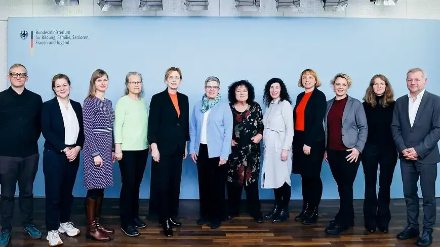 Eine Gruppe von zehn Personen aus bundeszentralen Organisationen der Senioren- und Pflegepolitik und die Bundesseniorenministerin Karien Prien steht lächelnd vor einer blauen Wand mit dem Logo des Bundesministeriums für Familie, Senioren, Frauen und Jugend. 