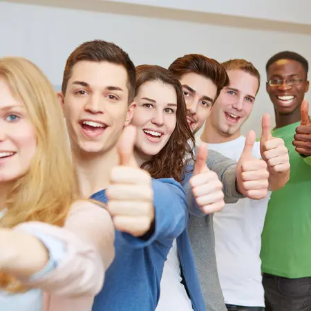 Eine Gruppe von sieben jungen Menschen steht in einer Reihe und lächelt. Alle halten ihre Daumen hoch, was Zustimmung oder Freude ausdrückt. Der Hintergrund ist hell und neutral gestaltet.
