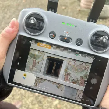 Image of a drone remote control. The remote control has a screen that displays the image from the drone camera. This image shows the facade of a historic building.
