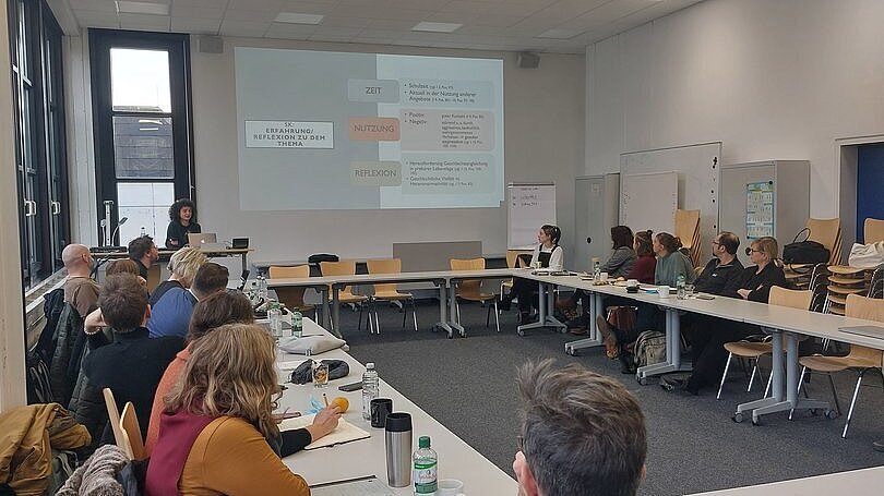 Vortag. Menschen sitzen in Tischen in einem Kreis 