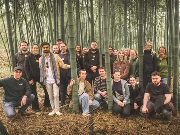 Eine Gruppe von 24 Personen steht in einem Bambuswald. Sie lächeln und posieren zusammen, während sie zwischen den hohen Bambusstämmen arrangiert sind. Die Atmosphäre ist freundlich und entspannt.