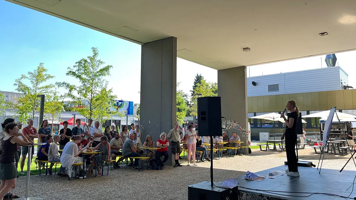 Prof. Dr. Maria Wiesmann steht auf einer Bühne. Ihr Publikum sitzt auf Biertischgarnituren