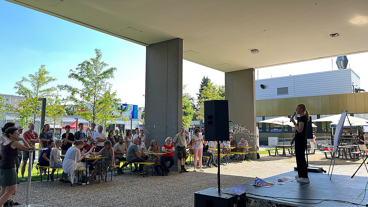 Prof. Dr. Maria Wiesmann steht auf einer Bühne. Ihr Publikum sitzt auf Biertischgarnituren