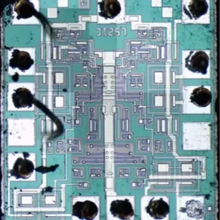 Bild eines Mikrochip-Layouts mit feinen Leiterbahnen und verschiedenen Verbindungsstellen. Die Hauptfarbe ist ein helles Blau mit grauen und weißen Elementen. Der Chip hat an den Ecken Löcher für Anschlüsse und zeigt komplexe Schaltkreismuster.