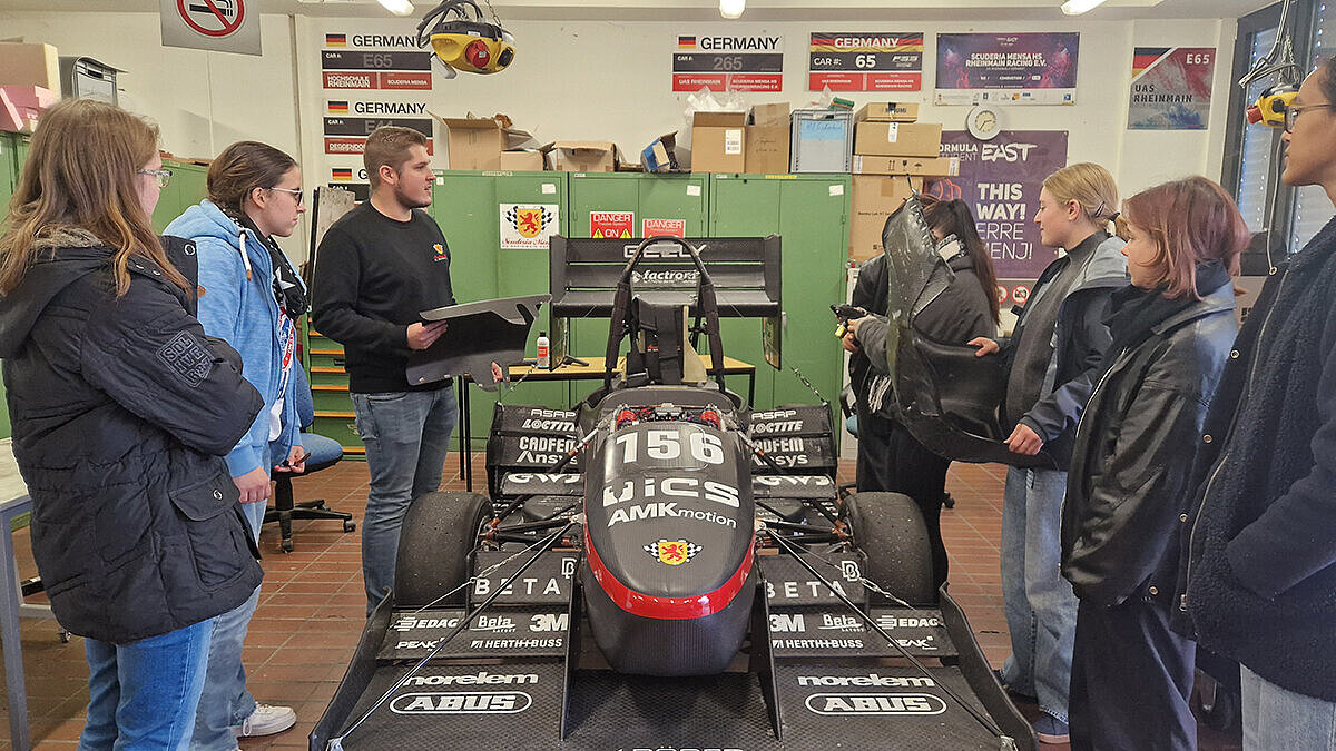 Die Teilnehmerinnen stehen in der Werkstatt des Formula Student Teams und betrachten das Rennauto Sandy