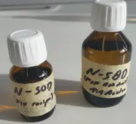 Zwei kleine braune Flaschen stehen nebeneinander. Beide haben weiße Schraubverschlüsse und sind mit einem Etikett versehen, auf dem "N-SD" steht. Die linksstehende Flasche ist kleiner als die rechtsstehende.