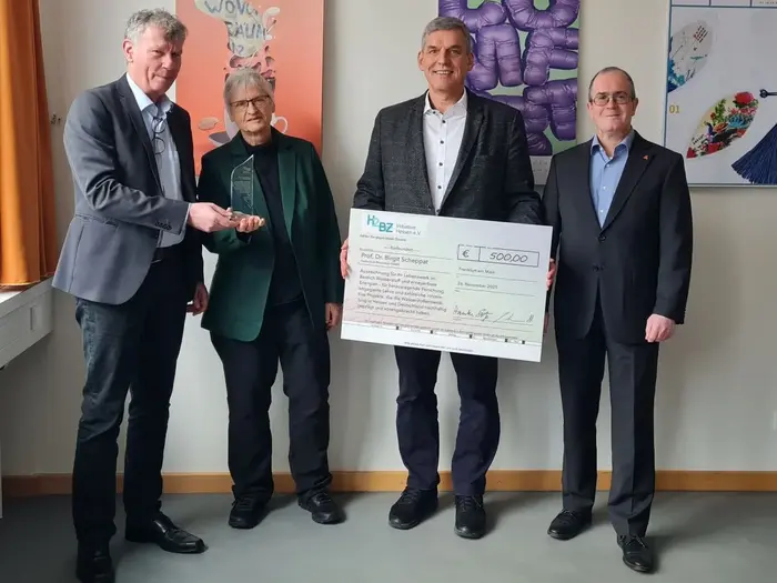 Vier Personen stehen in einem Raum und halten einen großen Scheck über 500 Euro. Die Personen scheinen sich über die Spende zu freuen, während sie in die Kamera schauen. Im Hintergrund sind Plakate und einige Dokumente an der Wand zu sehen.