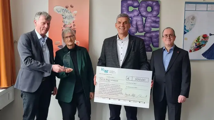 Vier Personen stehen in einem Raum und halten einen großen Scheck über 500 Euro. Die Personen scheinen sich über die Spende zu freuen, während sie in die Kamera schauen. Im Hintergrund sind Plakate und einige Dokumente an der Wand zu sehen.