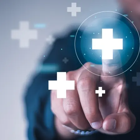 Eine Hand zeigt auf ein transparentes Pluszeichen vor einem unscharfen Hintergrund. Weitere Pluszeichen sind um die Hand herum angeordnet, was eine digitale oder positive Interaktion symbolisiert.