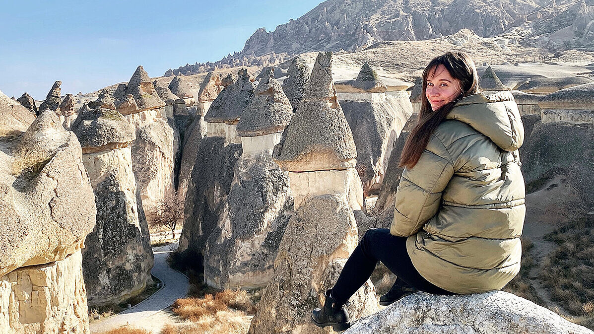 Clara Draskoczy Clara Draskoczy sitzt auf einem Felsen vor einer steinigen Landschaft und lächelt in die Kamera