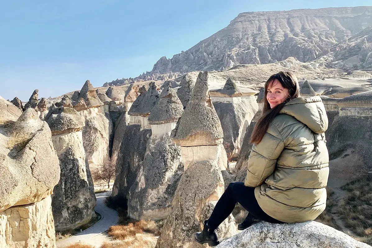 Clara Draskoczy sitzt auf einem Felsen vor einer steinigen Landschaft und lächelt in die Kamera
