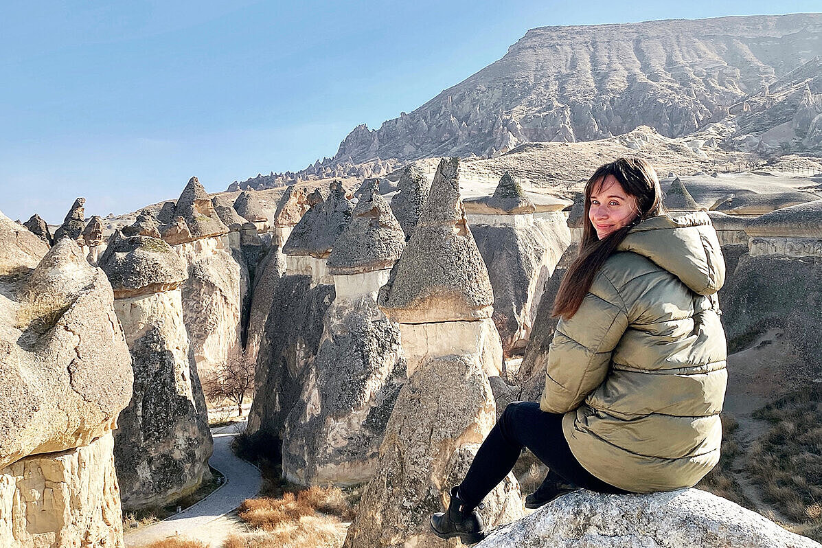 Clara Draskoczy Clara Draskoczy sitzt auf einem Felsen vor einer steinigen Landschaft und lächelt in die Kamera