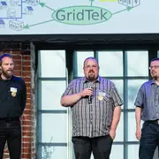 Drei Männer stehen auf einer Bühne und präsentieren ihr Projekt "GridTek"