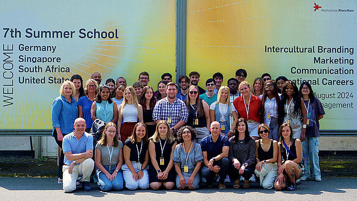 Gruppenfoto mit allen Beteiligten vor einer Werbeplakatwand für die Summer School.