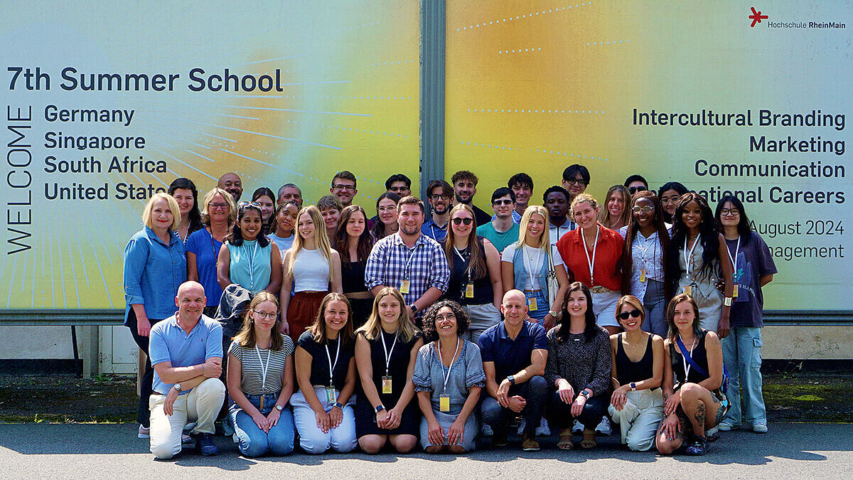 Gruppenfoto mit allen Beteiligten vor einer Werbeplakatwand für die Summer School.