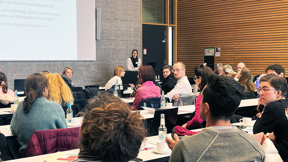 Die Teilnehmenden des Workshops sitzen in einem Saal an langen Tischreihen 