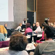 Die Teilnehmenden des Workshops sitzen in einem Saal an langen Tischreihen 