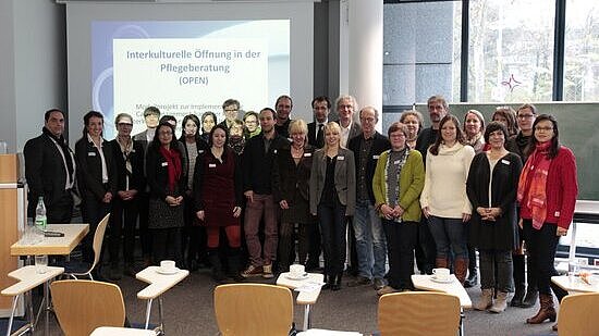 Das Team des Projekts OPEN steht in einem Klassenraum der Hochschule RheinMain vor einer Präsentation des Projektes.
