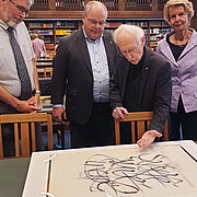 Dr. Martin Mayer (Hochschul- und Landesbibliothek RheinMain), Prof. Dr. Andreas Brensing (HSRM), Prof. Gottfried Pott und Felicitas Reusch (1. Vorsitzende Kunstarche Wiesbaden e. V.) betrachten ein kalligrafisches Werk von Prof. Gottfried Pott 