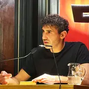 Poetikdozent Necati Öziri sitzt an einem Tisch und liest aus seinem Buch, das vor ihm liegt