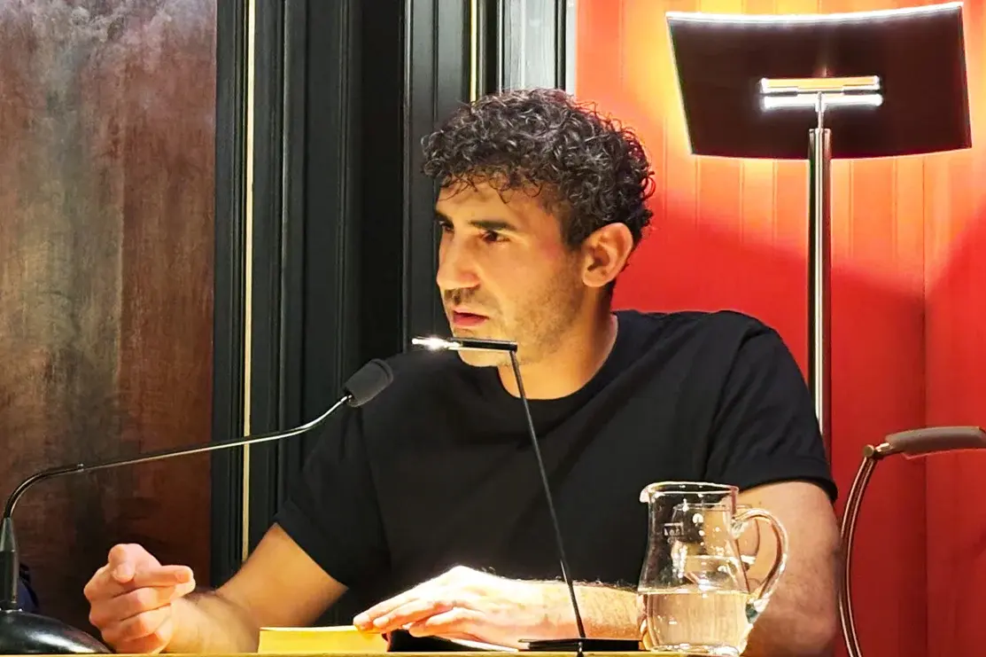 Poetikdozent Necati Öziri sitzt an einem Tisch und liest aus seinem Buch, das vor ihm liegt