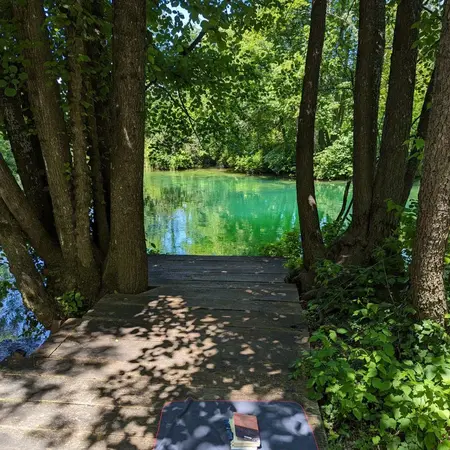 Entspannt lesen am Fluss in Bellavici, Kroatien Es ist ein Holzsteg zu sehen, auf dem ein Handtuch mit Buch und HSRM-Tasche liegt. Ein türkiser Fluss im Hintergrund schimmert in der Sonne
