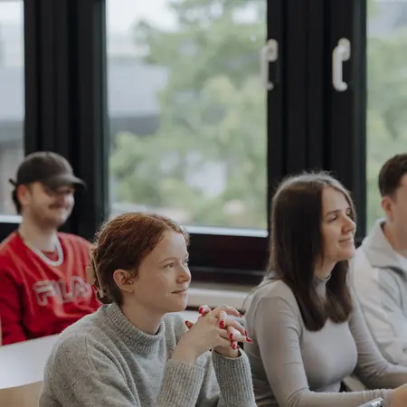 Man sieht mehrere Studierende, die gespannt nach vorne schauen und dem Kurs zuhören. Sie sitzen an Schreibtischen und haben ihre Tablets vor sich. Im Hintergrund sieht man große Fenster und die Natur dahinter.