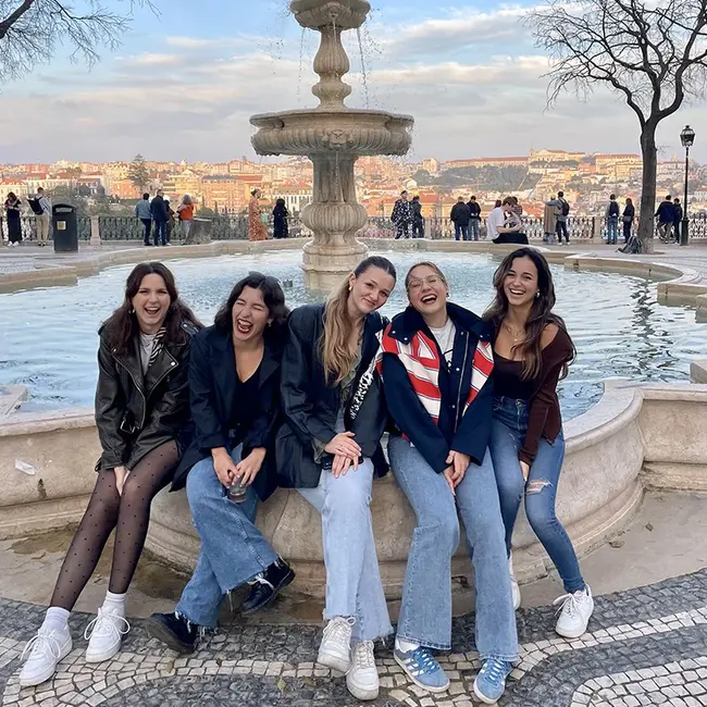 Sarah Faust sitzt mit Freund:innen in Lissabon am Rand eines Springbrunnens