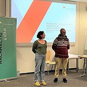 Zwei studentische Mitarbeitende des Nachhaltigkeitsbüros stehen vor den Anwesenden, neben ihnen steht auf einem Banner "Nachhaltig @ HSRM"