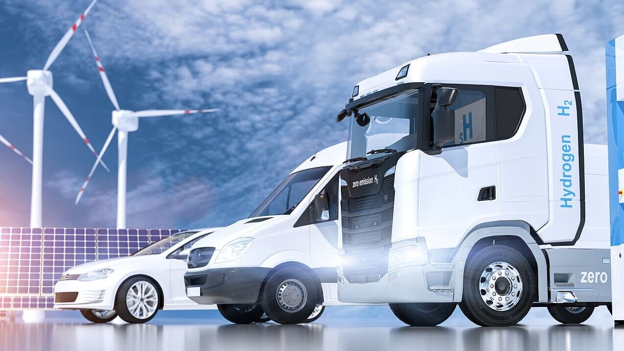 E-Mobilität E-Lkw, E-Transporter und E-Pkw mit Windrädern und Photovoltaik im Hintergrund