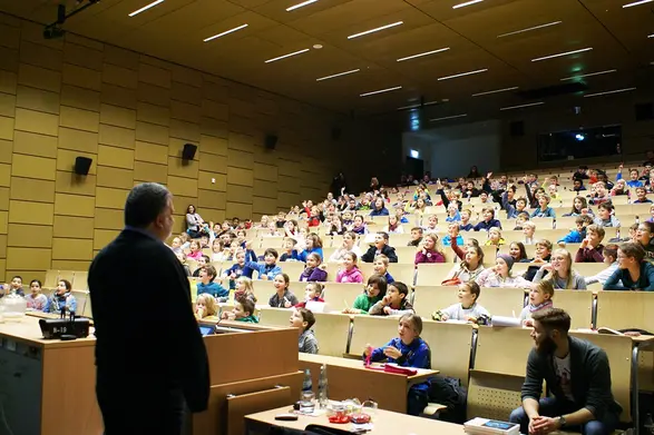 Blick in den Audimax am Rüsselsheimer Campus, vollbesetzte Stuhlreihen mit Kindern, Prof am Rednerpult