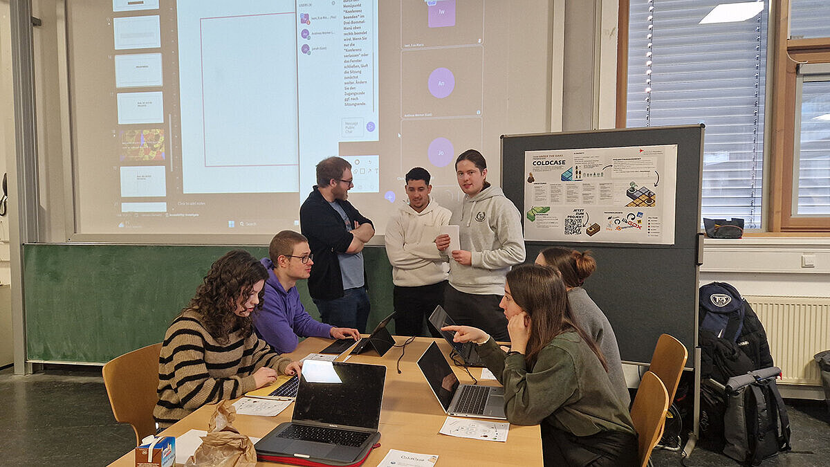 Studierende sitzen an einem Projektstand an einem Tisch und testen das Spiel "Cold Case"
