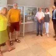 Fünf Personen stehen zusammen in einem Innenraum vor einer Vitrine. Die Gruppe besteht aus zwei Frauen und drei Männern, die in verschiedenen farbigen Outfits gekleidet sind. Die Vitrine im Hintergrund enthält verschiedene Ausstellungsstücke.