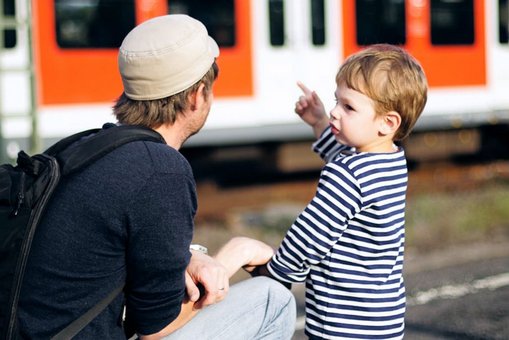 Vater mit seinem Sohn an einem Bahnsteig mit einem Zug im Hintergrund