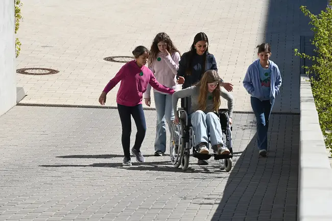 Fünf Teilnehmerinnen am Girls’Day 2026 unterstützen ein Mädchen im Rollstuhl, während sie eine Rampe hinunterfahren.