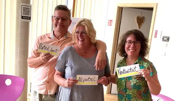 Drei Personen stehen zusammen in einem Raum. Sie halten Schilder mit den Aufschriften "Partizipation", "Allpartizipation" und "Neutralität". Die Atmosphäre wirkt freundlich und engagiert, vermittelt ein Gefühl von Zusammenhalt und gemeinsamer Arbeit.