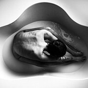 Ein Schwarz-Weiß-Foto zeigt einen sitzenden Menschen in einer halbvollen, rundgeschwungenen Badewanne, fotografiert aus der Vogelperspektive. 