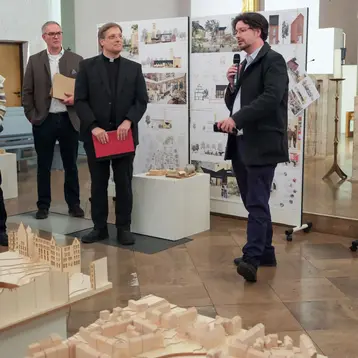 Prof. Dr. Christian Schachtner gives a welcoming speech for the Böttiger Prize 2025. He stands between the models and plans of the architecture students.