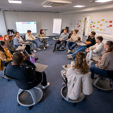 Studierende sitzen auf Stühlen in einem Kreis während eines Workshops