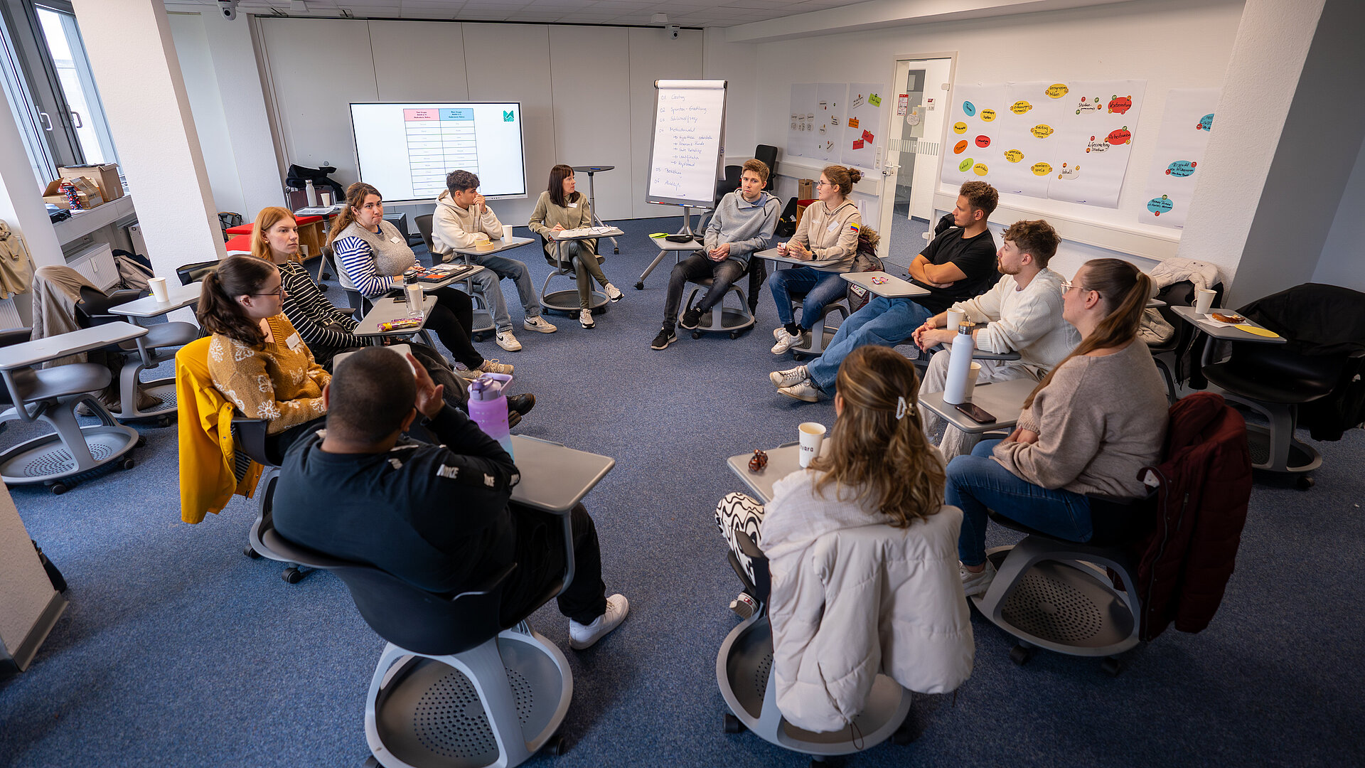 Studierende sitzen auf Stühlen in einem Kreis während eines Workshops