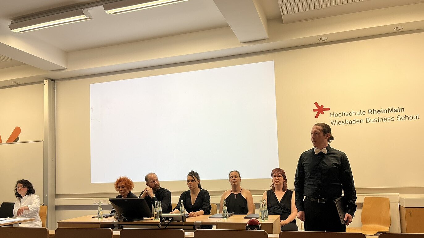 Theaterlesung Menschen sitzend und stehend vor einer Leinwand
